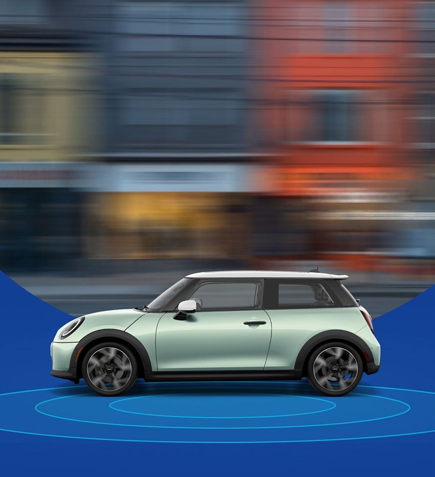 The side-view of a Mini Cooper Hardtop 2 Door with a blurred city street in the background and blue rings beneath it.