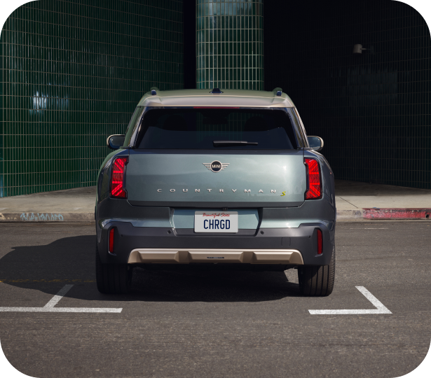 Three-quarters front view of a MINI Electric vehicle   parked on a cobblestone surface in a parking space in   front of a retail storefront in an urban setting.